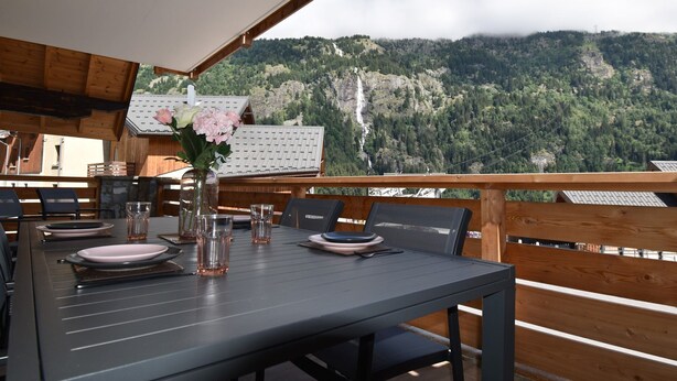A dining table set with plates, glasses, and a vase of flowers, overlooking a mountainous landscape. - L'Étendard appartement 5 (Vaujany)