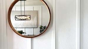 A mirror with a wooden frame, two patterned ottomans, a hanging light fixture, and a wall-mounted plant. - Updated Great Location Beautiful New House (Thornton)