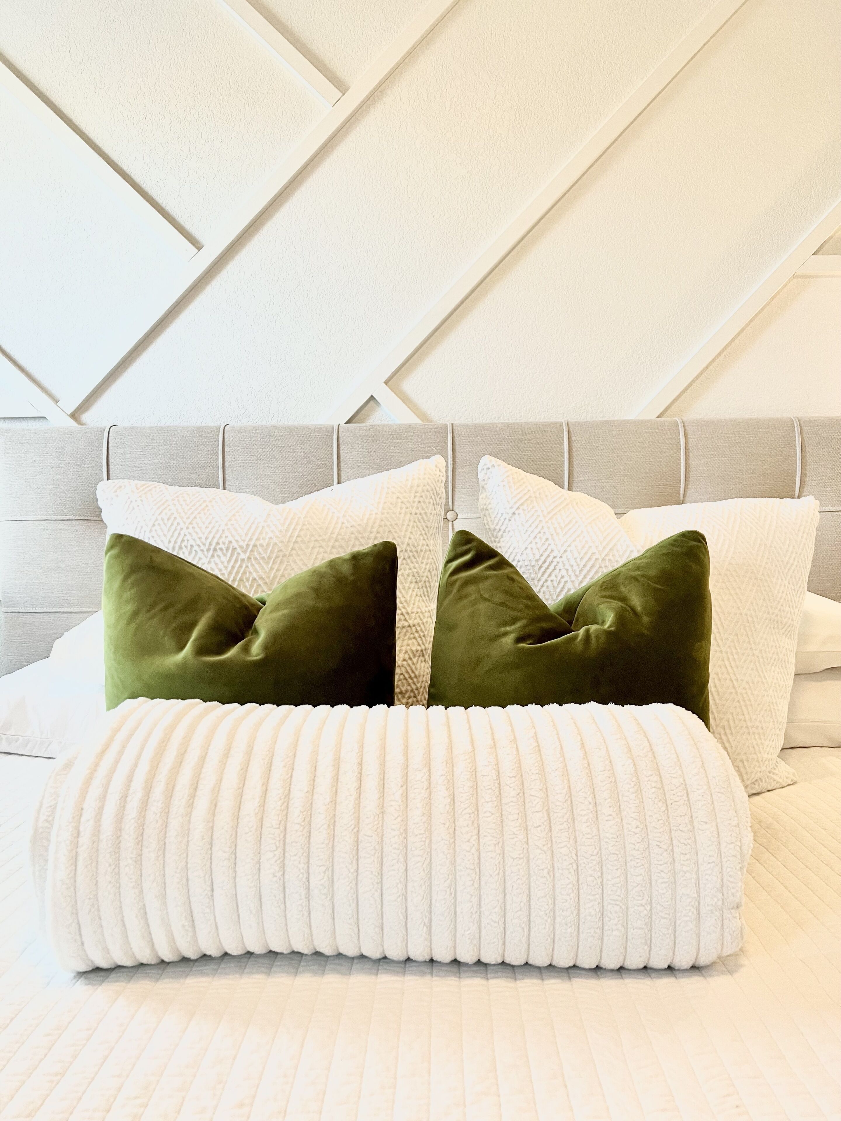 Un lit bien fait, agrémenté d’un arrangement d’oreillers blancs et verts, d’une tête de lit grise et d’un mur à motifs.