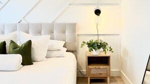 A modern bedroom with a large bed, a bedside table with a plant, and a wall-mounted clock. - Updated Great Location Beautiful New House (Thornton)