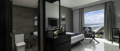 A modern hotel room with a large bed, a sitting area with a view, a bathroom, and a minibar.