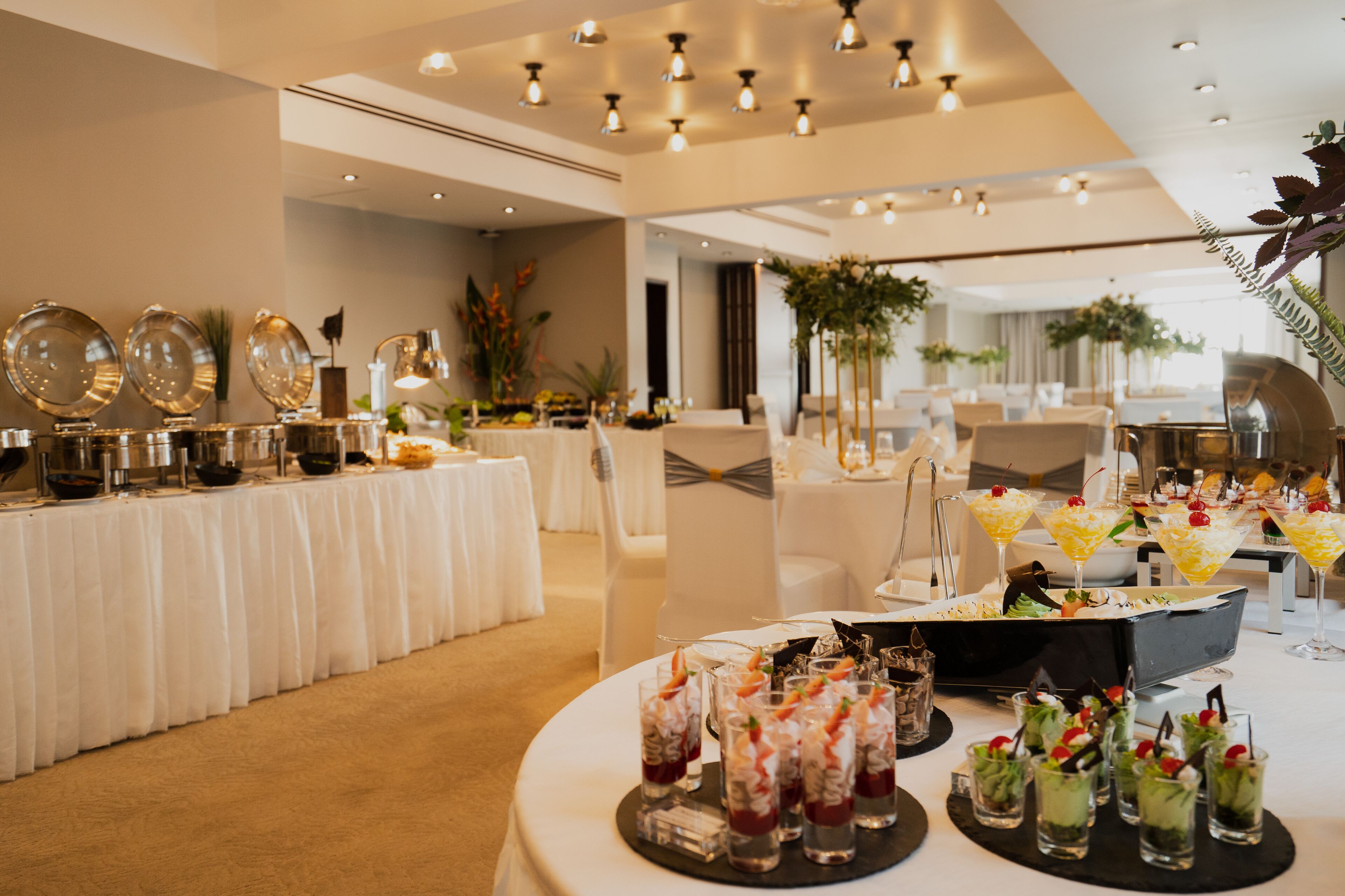 Un salón de banquetes con mesas redondas dispuestas para un evento formal, que ofrece una variedad de comida y bebidas.