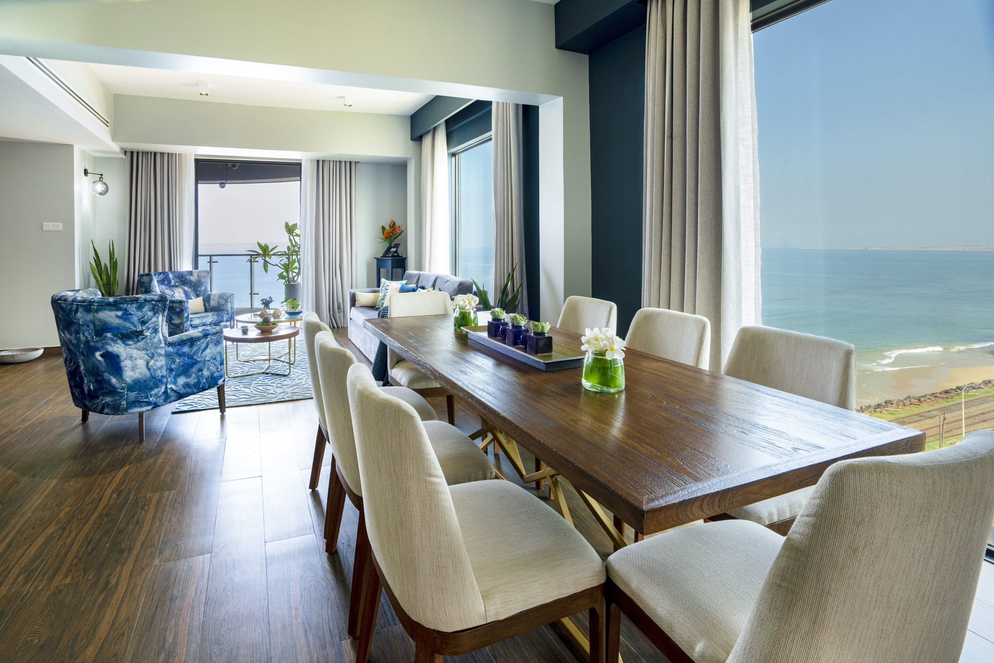 A modern dining area with a wooden table and chairs, a sofa, and a view of the ocean.