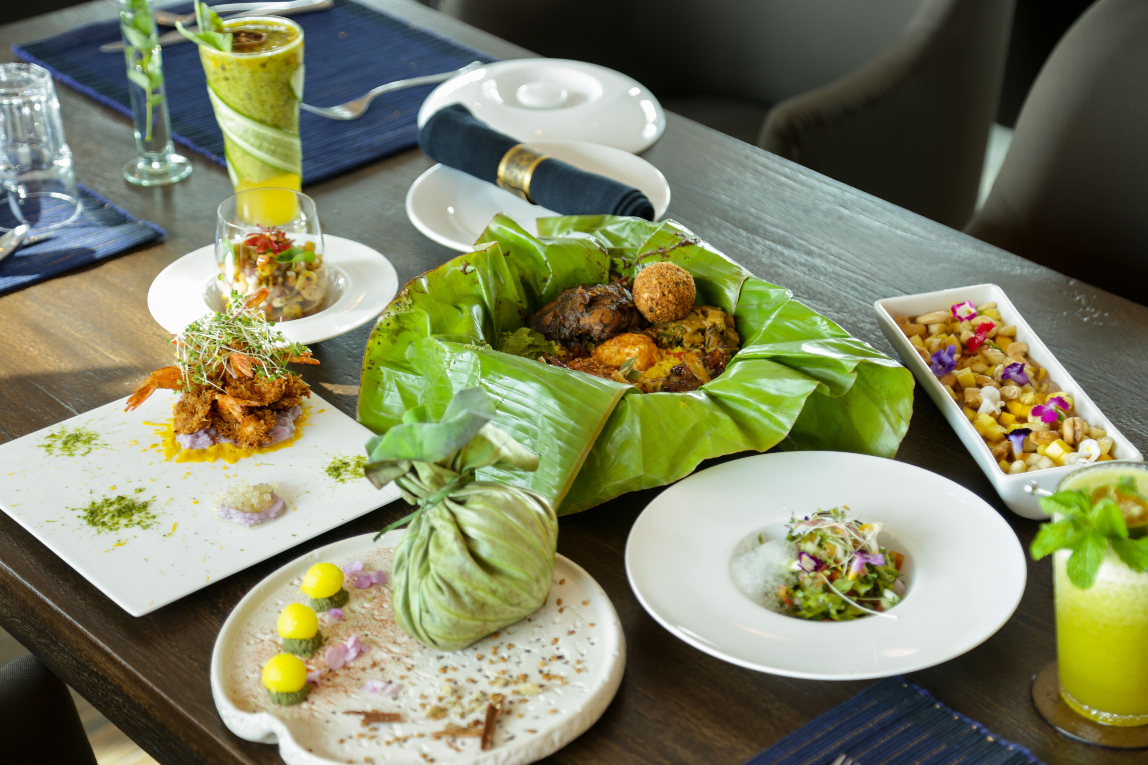 Een eettafel met diverse gerechten, waaronder een salade, een schaal noten en een bord met een groene bladwrap.