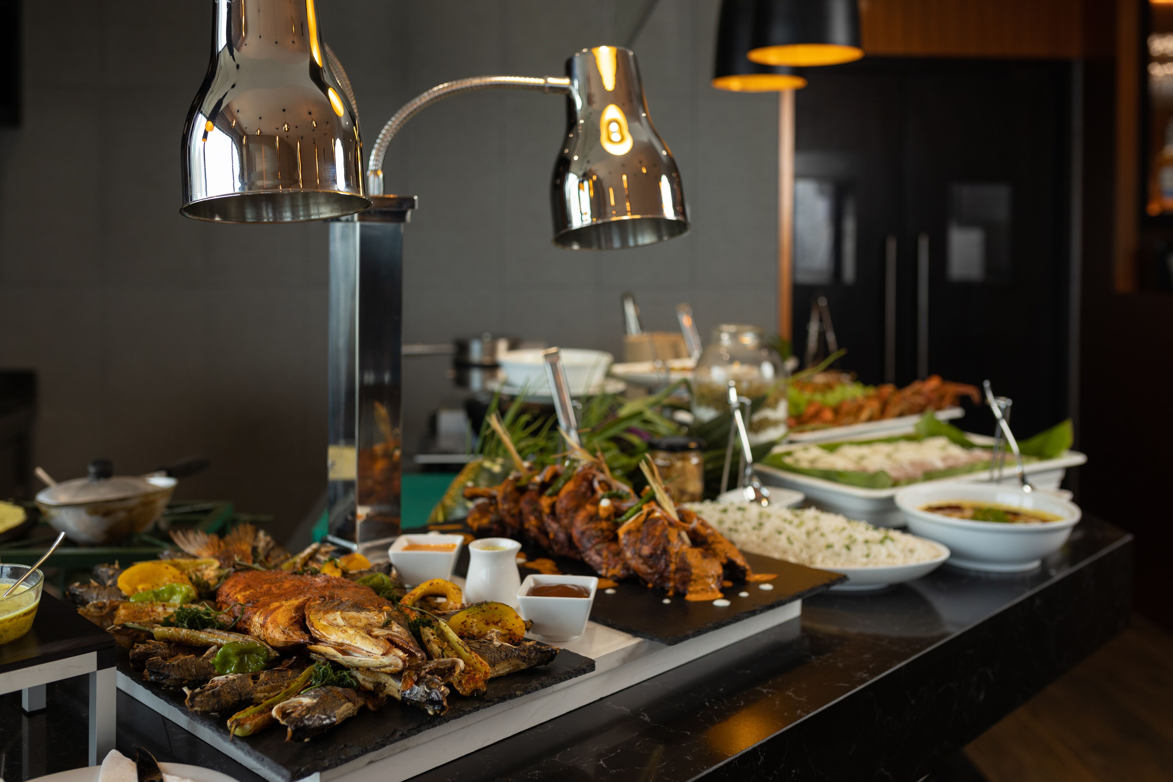 Un bufé con diversos platos, incluyendo mariscos y arroz, y dos lámparas colgantes arriba.