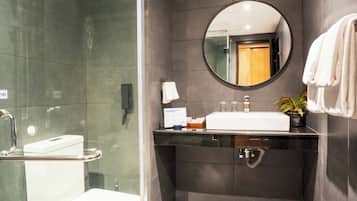 A modern bathroom with a glass-enclosed shower, a white sink, a round mirror, and a dark tiled wall.