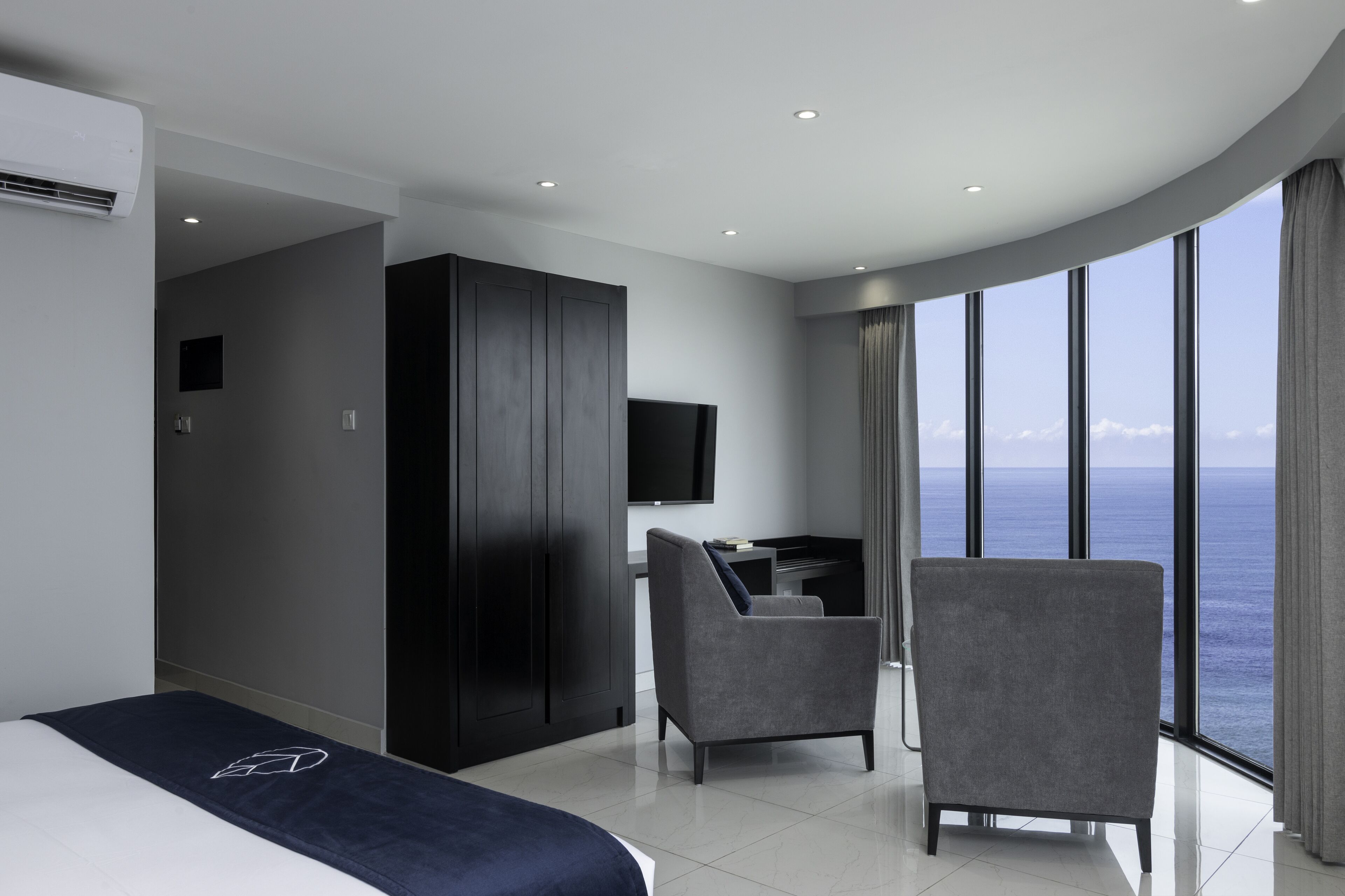 Ein modernes Hotelzimmer mit Bett, Schreibtisch, Stuhl und einem großen Fenster mit Blick auf den Ozean.