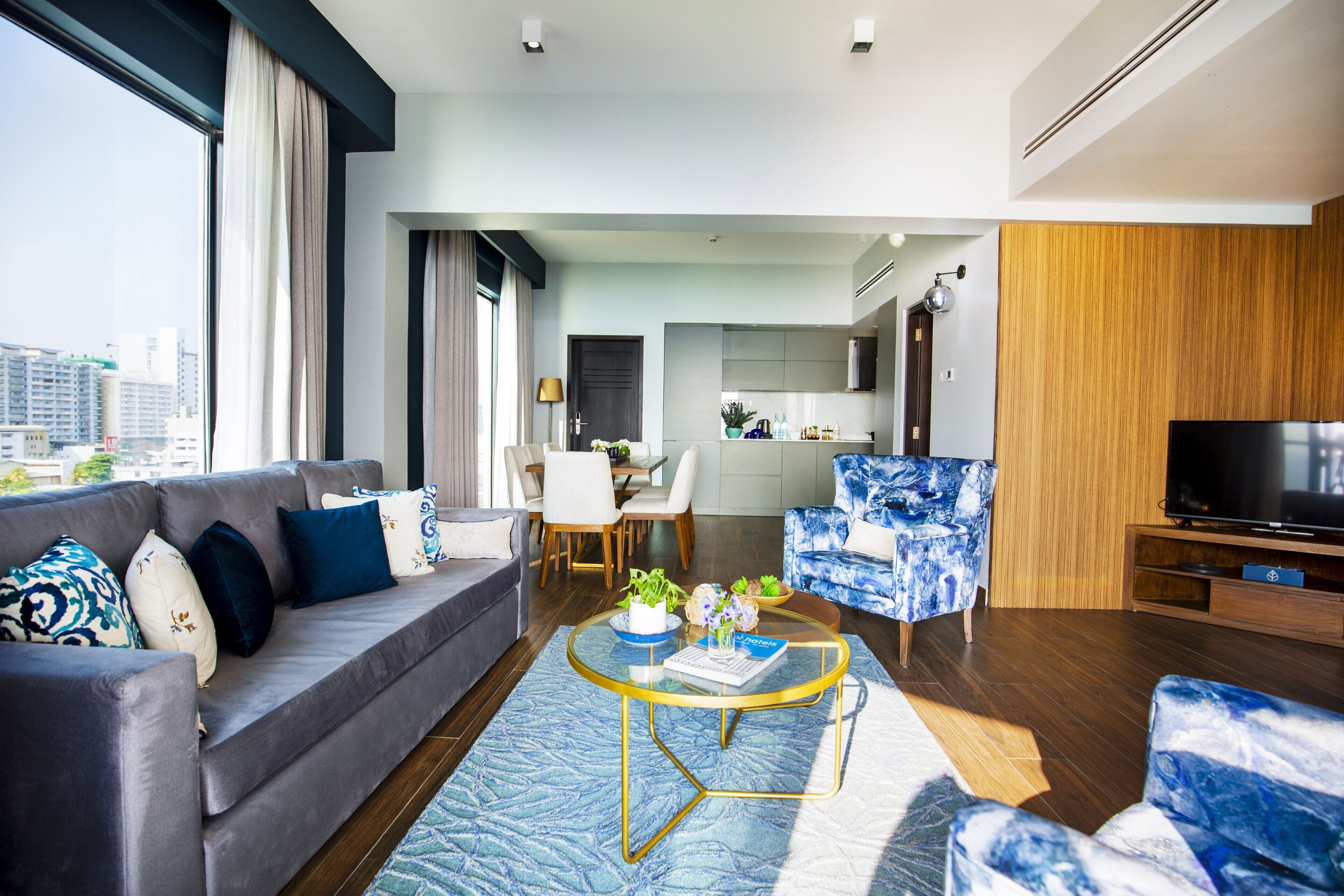A modern living room with a grey sofa, blue patterned armchair, and a coffee table with a book and plants.