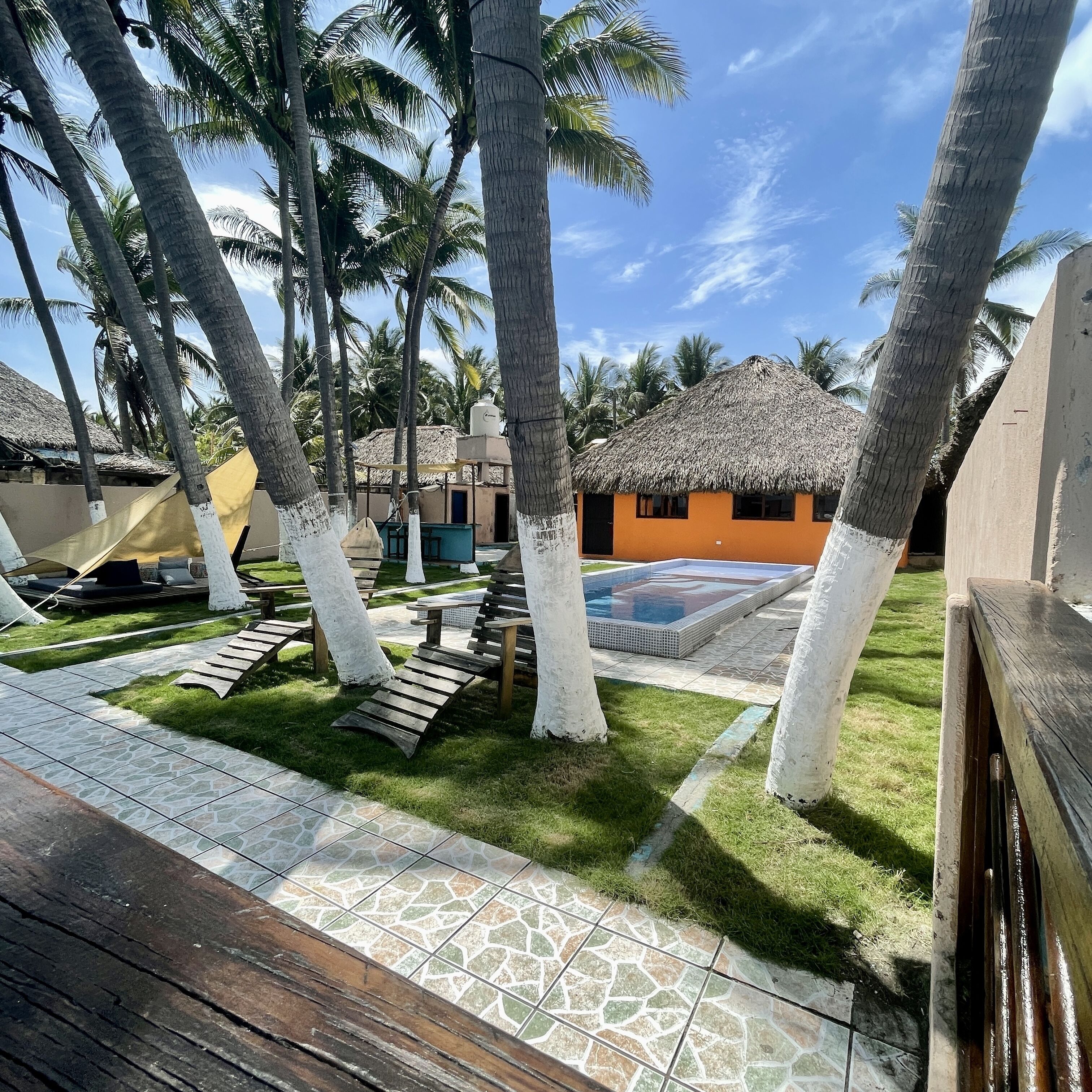 A tropical resort with palm trees, a swimming pool, and thatched-roof buildings.