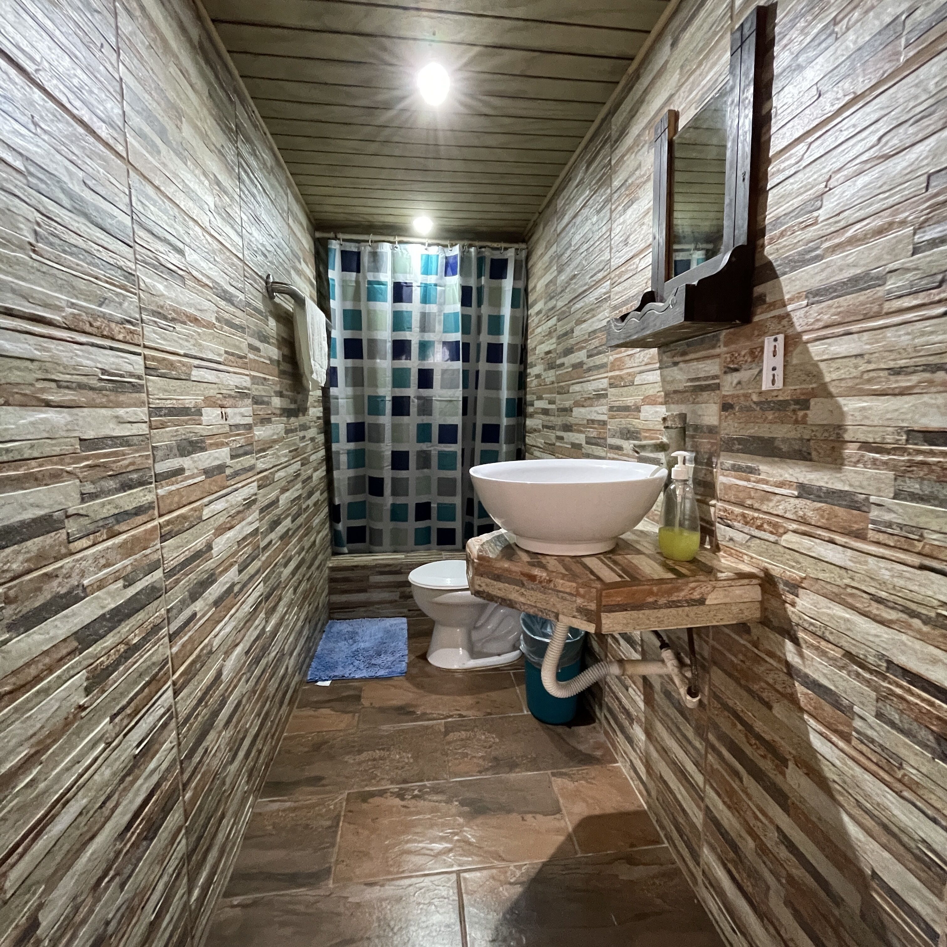 A narrow bathroom with a stone wall design, a white sink, and a toilet.