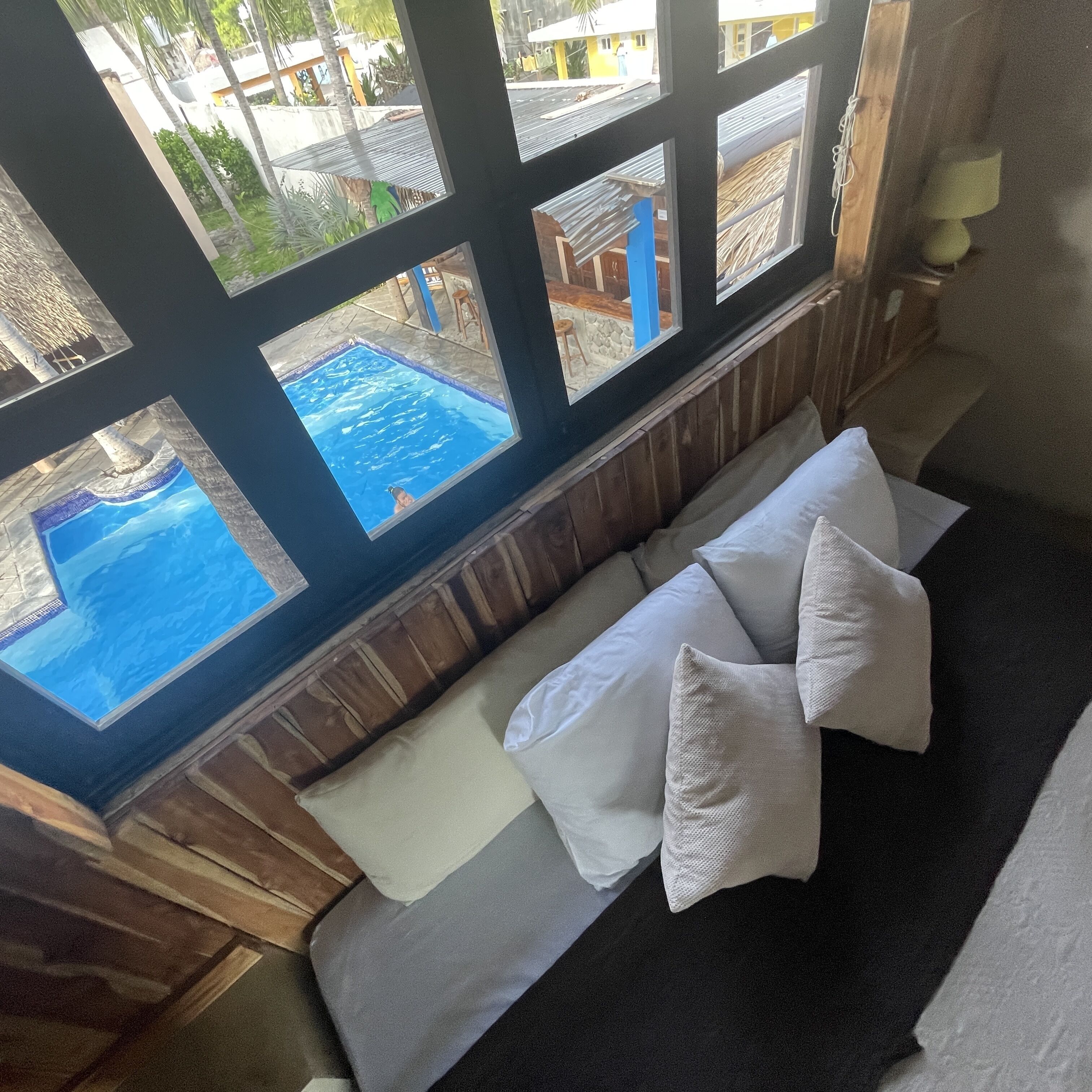 Une pièce avec vue sur une piscine, grâce à de grandes fenêtres. On y trouve un banc rembourré avec des coussins.