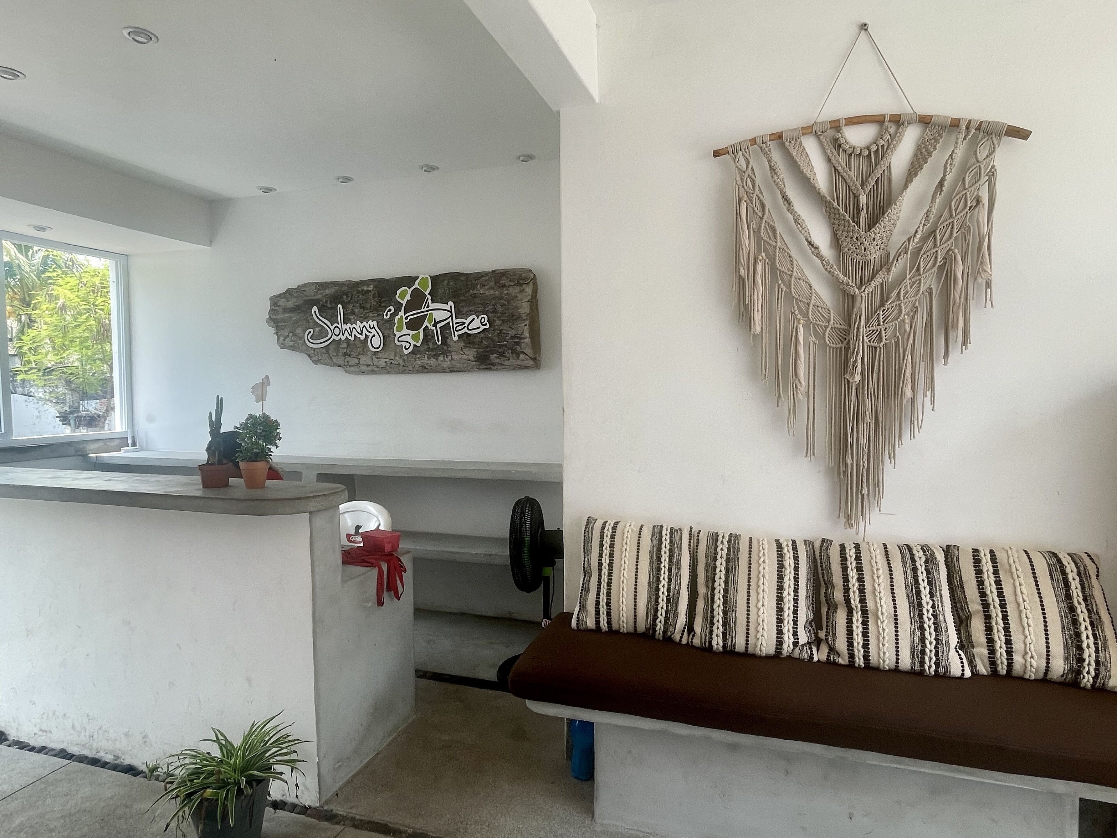 A modern living area with a sofa, a macrame wall hanging, and a sign that reads "Johnny Place".