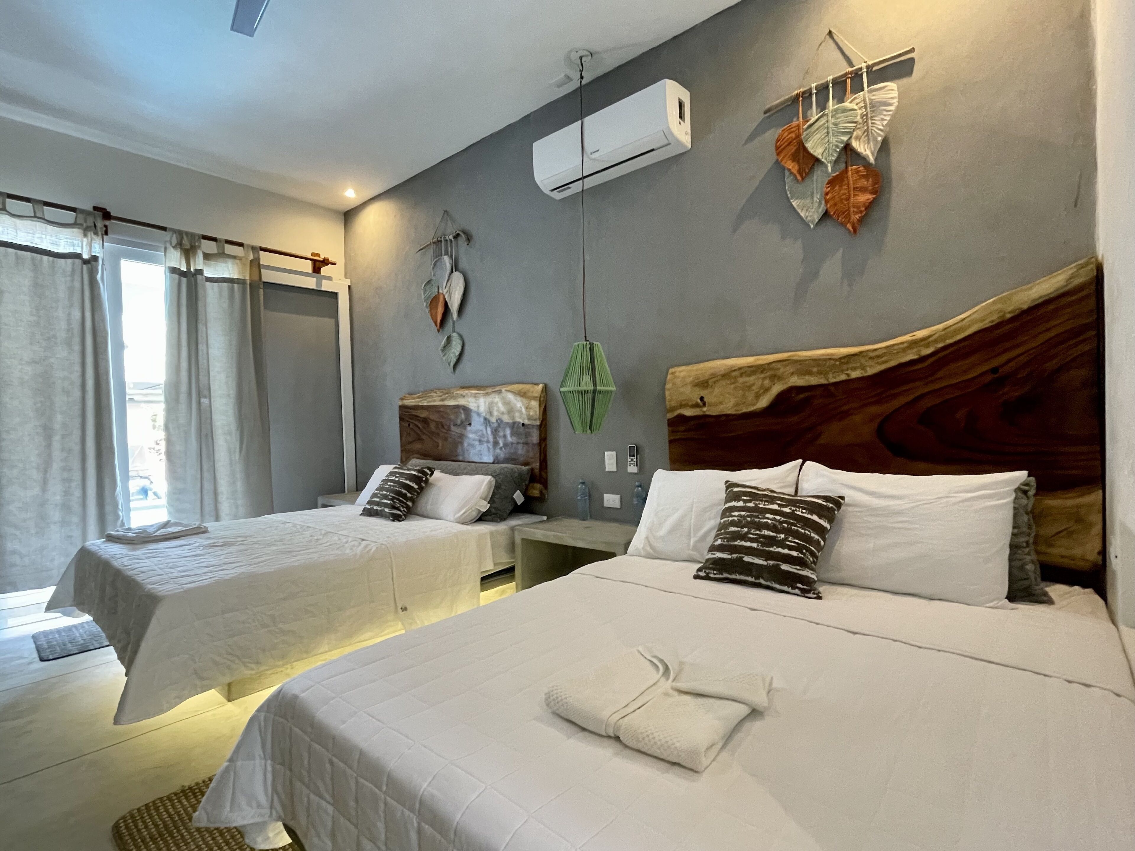 Habitación de hotel con dos camas, cabecero de madera, aire acondicionado y vistas al exterior.
