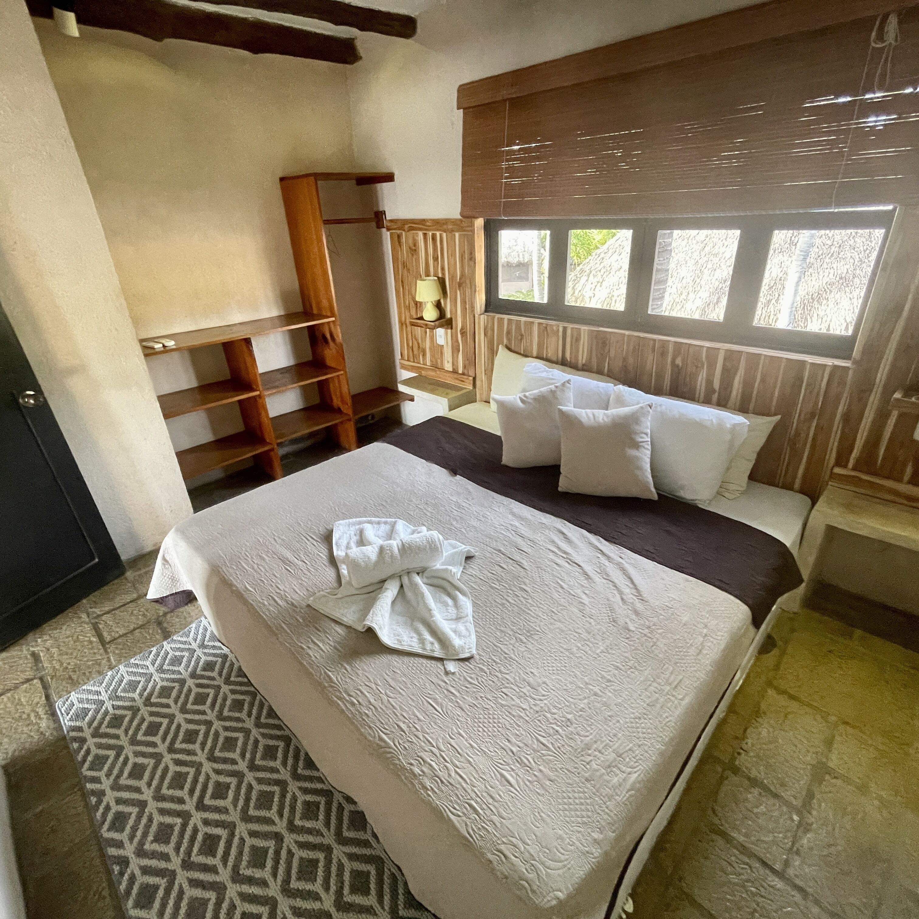 A neatly made bed with pillows and a towel, a wooden ladder, and a window with blinds.