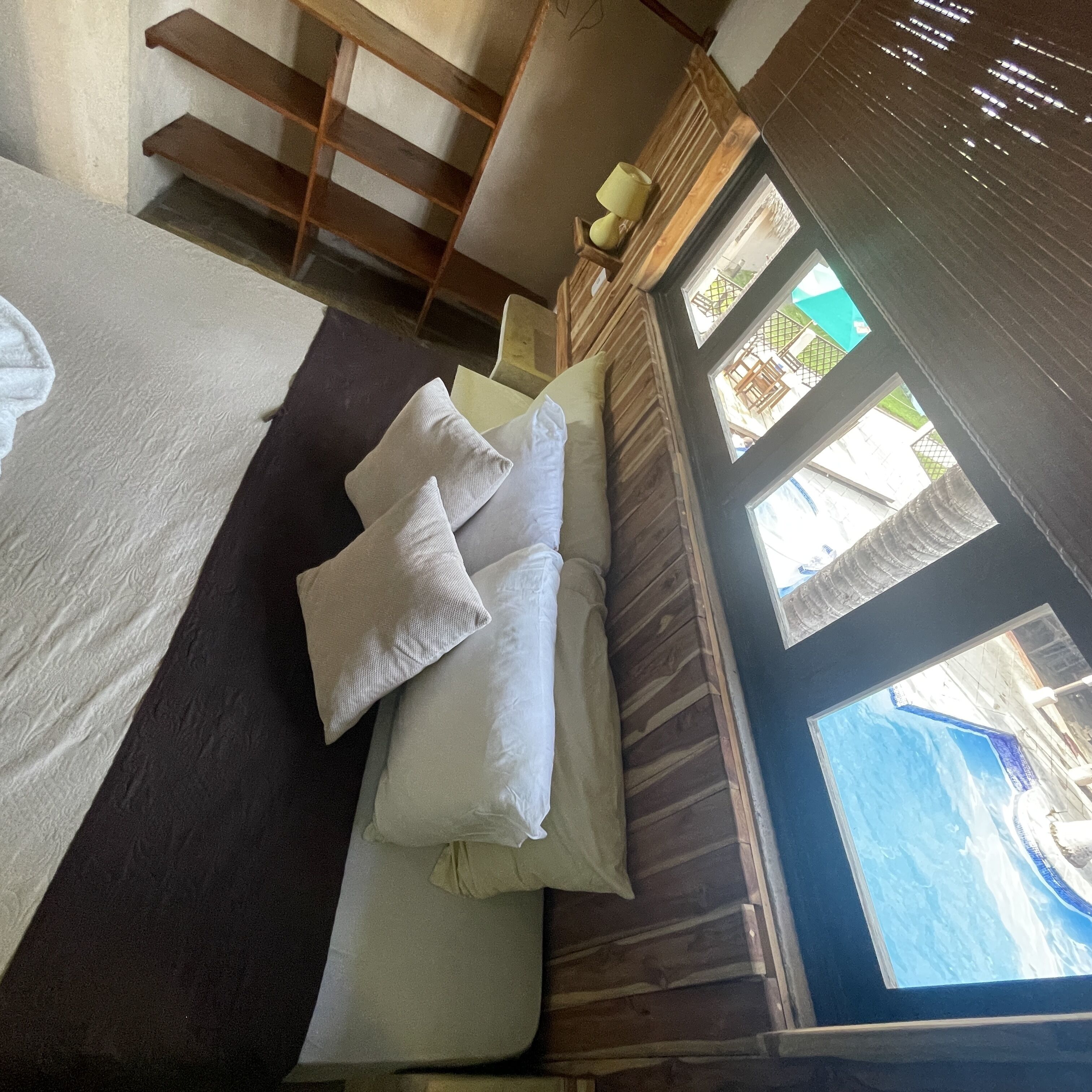 A bed with pillows and a blanket, wooden headboard, and a window with a view of a building.