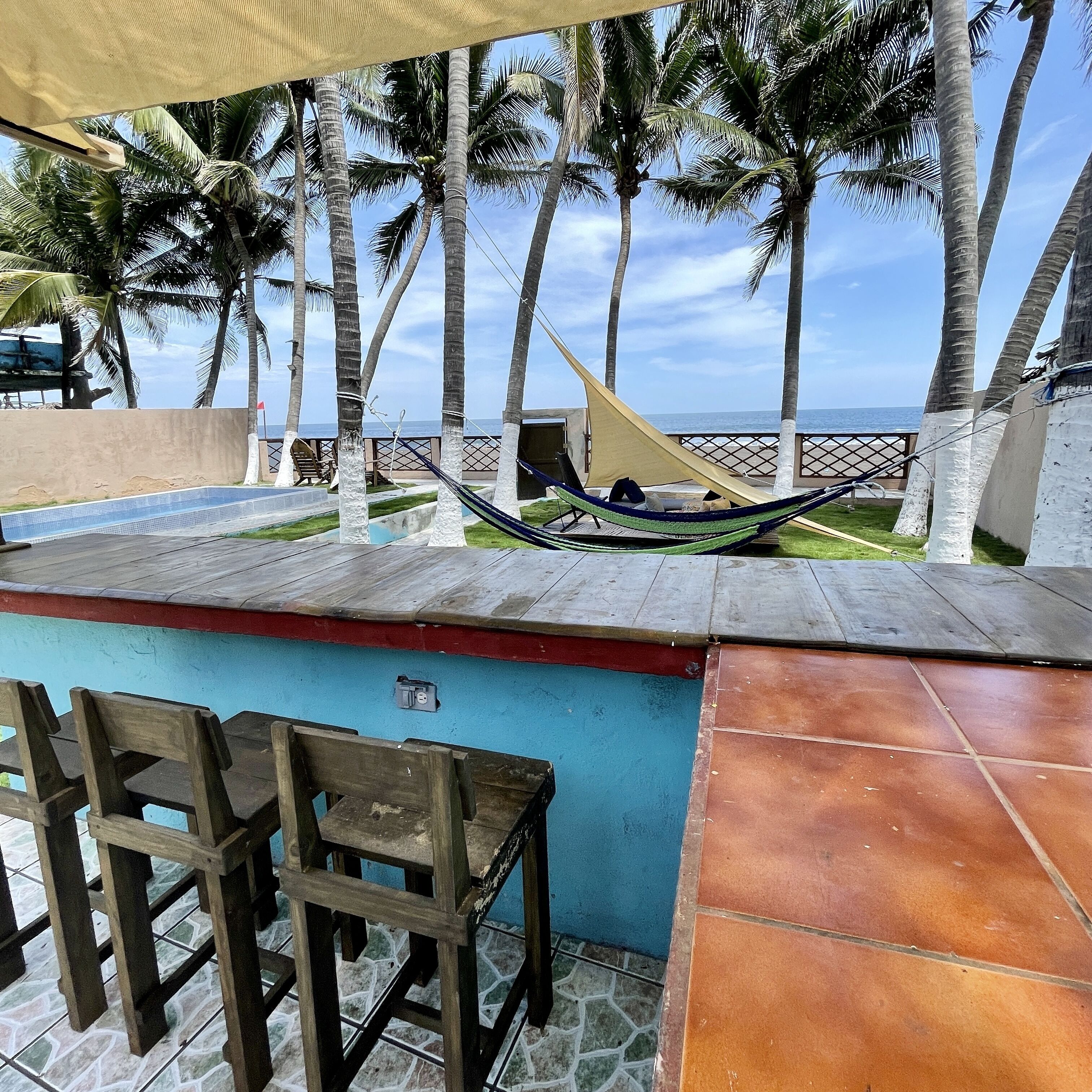 A poolside area with a hammock, wooden chairs, and a view of the ocean.
