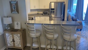 Una cucina moderna con mobili bianchi, un frigorifero in acciaio inossidabile e un'area bar con tre sgabelli.
