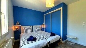 Une chambre avec deux lits, une fenêtre, un radiateur, une lampe de chevet et une petite table ronde.