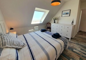 Une chambre avec un puits de lumière, un lit avec une literie à rayures, une commode blanche et une chaise.