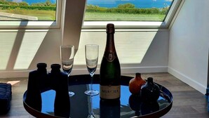 Une table avec une bouteille de champagne Mercier, deux verres et un petit vase, le tout placé sur un balcon offrant une vue panoramique sur la mer et la verdure.