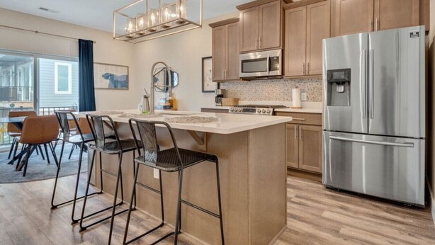 A modern kitchen with a central island, stainless steel appliances, and a dining area with bar stools.