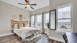 A bedroom with a bed, a ceiling fan, a window, and a view of a building outside.