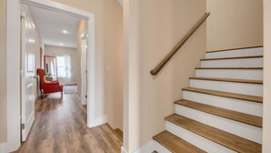 A hallway with wooden flooring, a red chair, and a staircase with wooden steps and a wooden handrail.