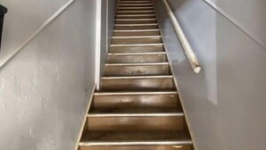 Uma escadaria com grades e corrimão de metal, que leva a um patamar com luminária.