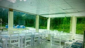 Amplo espaço interno com paredes de vidro, mobiliário branco e vista para uma área arborizada.