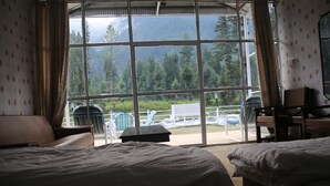 Quarto de hotel com duas camas, uma escrivaninha e vista para uma paisagem montanhosa através de amplas janelas.