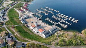 Vue aérienne d’une marina avec des bateaux amarrés, un petit bâtiment doté d’un toit rouge et des quartiers résidentiels environnants.