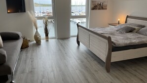 Une chambre avec un lit, une télévision, une fenêtre donnant sur les bateaux et un tableau au mur.