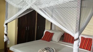 Een bed met houten frame, witte beddengoed en een wit hemeltje.