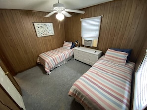 A bedroom with two beds, a dresser, a ceiling fan, a framed fish chart, and a window with blinds.