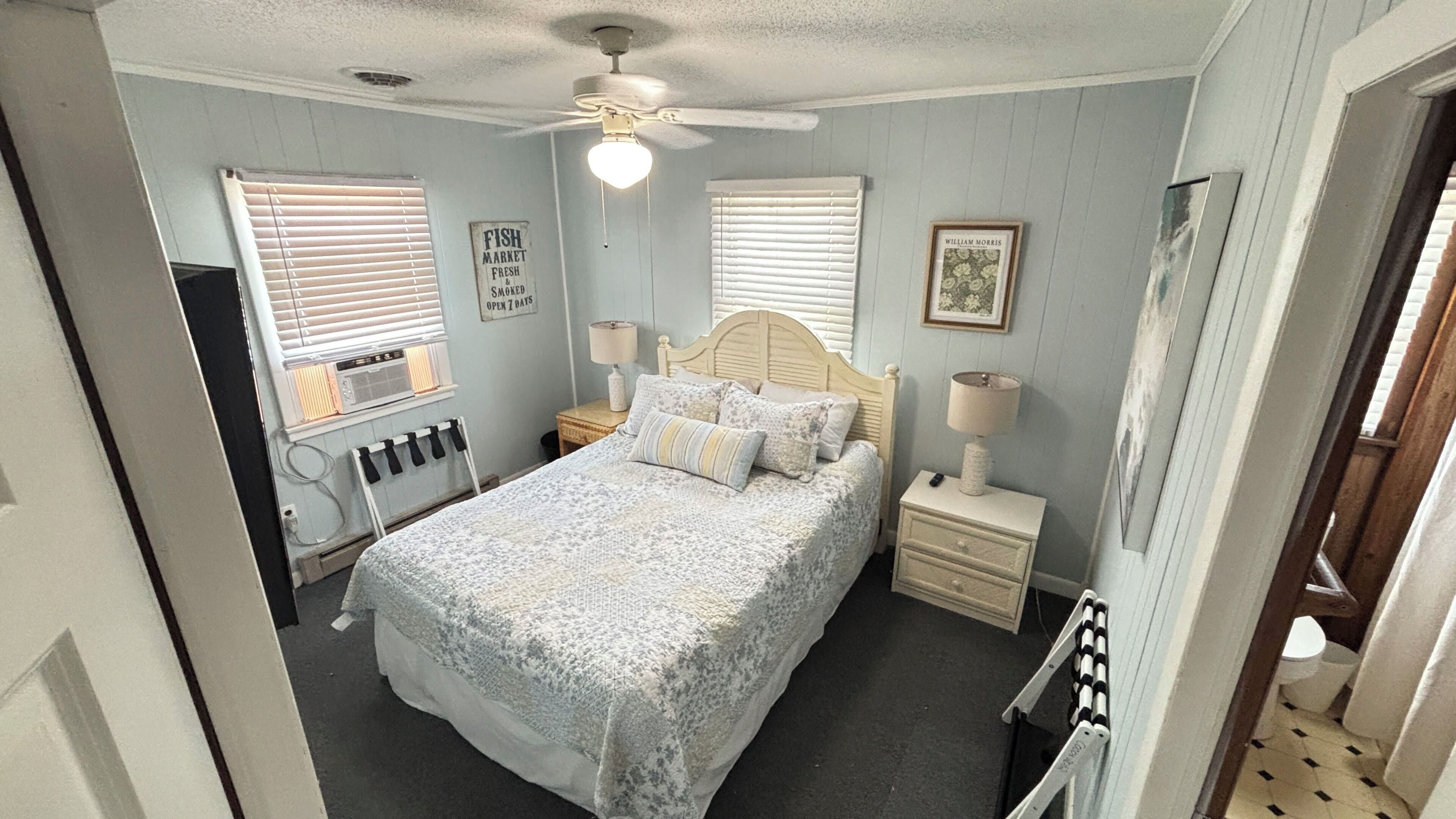 Une chambre à coucher comprenant un lit, deux tables de chevet, un ventilateur de plafond et un radiateur.