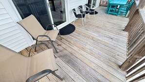 A wooden deck with outdoor furniture, a sliding glass door, and a view of neighboring houses. - DOGS AND DAY DREAMS! August & September dates available (Kill Devil Hills)