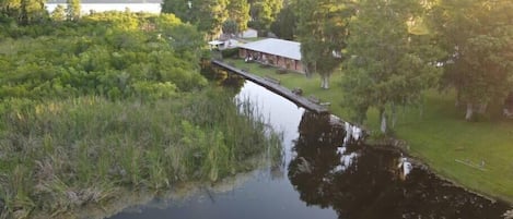 En stuga vid floden med en brygga som sträcker sig ut i vattnet, omgiven av tät vegetation och träd.