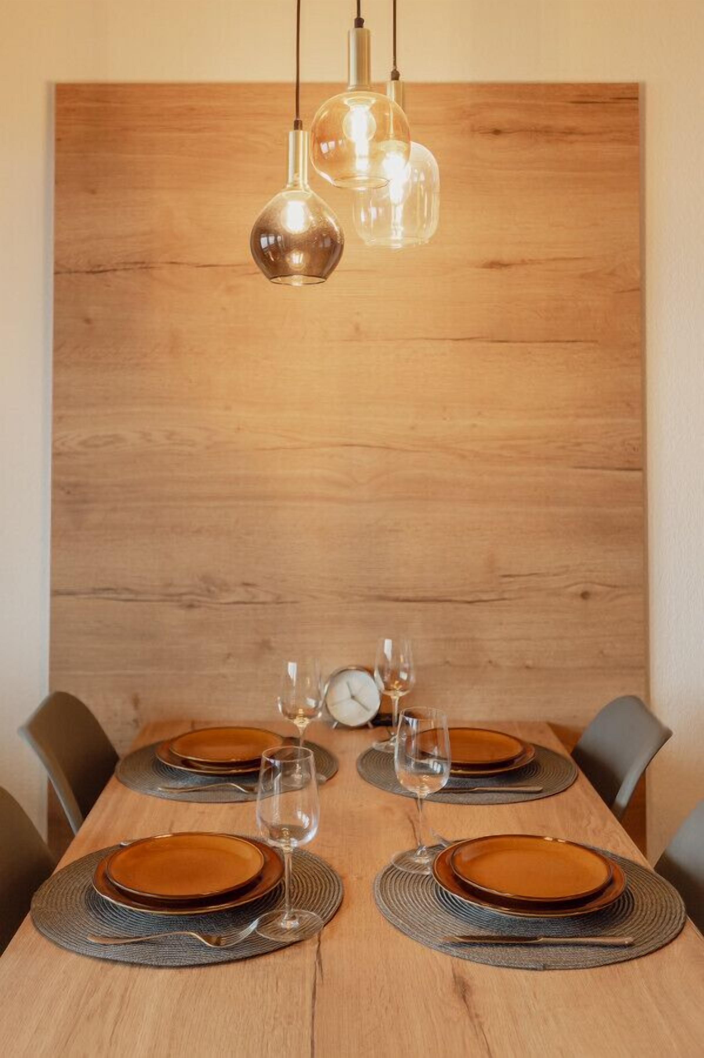 Une table à manger dress ée avec des assiettes, des verres et des couverts, le tout placé devant un mur en bois et éclairé par des suspensions.