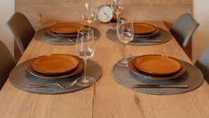Mesa de jantar posta com pratos, copos e talheres, com parede de madeira e luminárias pendentes acima.