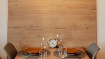 Ein Esszimmertisch ist mit Tellern, Gläsern und Besteck gedeckt, mit einer Holzwand und Pendelleuchten darüber.