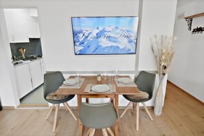 A dining area with a wooden table set for four, a kitchen in the background, and a framed picture on the wall. - New studio with a breathtaking view of the valley (Leukerbad)