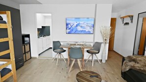 Un saló modern amb zona de menjador, cuina de fons i un televisor gran penjat a la paret.