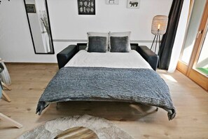 A bedroom with a bed, two bedside tables, a floor lamp, and a mirror on the wall. - New studio with a breathtaking view of the valley (Leukerbad)