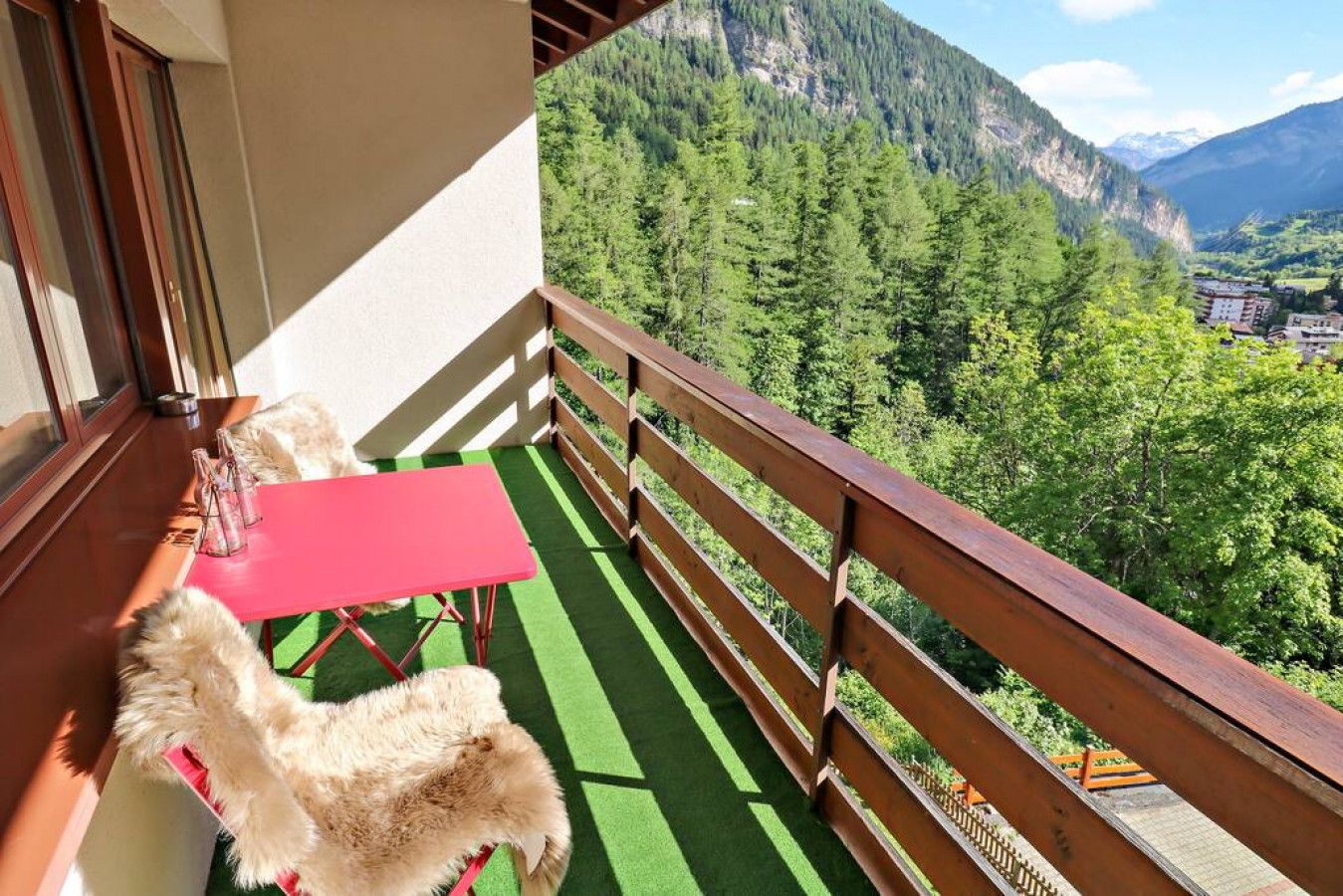 A balcony with a red table and chairs, overlooking a mountainous landscape.
