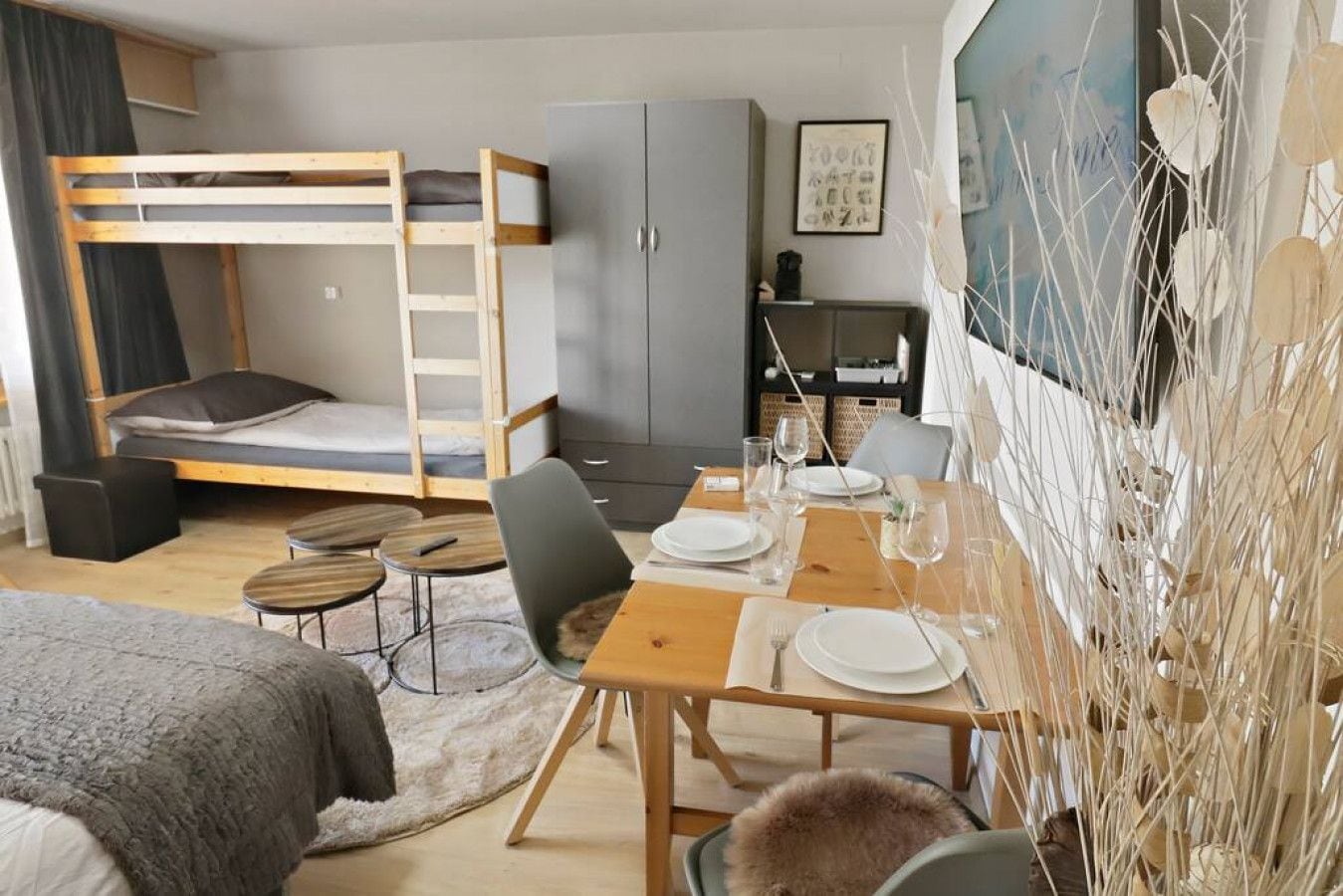 Una habitación moderna y funcional con una cama litera, una mesa de comedor para dos personas, una pequeña cocina y un adorno en la pared.