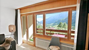 Habitació amb finestra gran que dona a un paisatge de muntanya, un radiador, una cadira i un sofà cobert de pell.