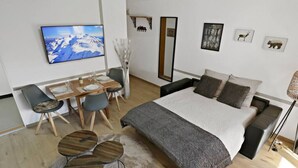 Un dormitori modern amb un llit gran, una taula de dinar amb caires i un televisor fixat a la paret.