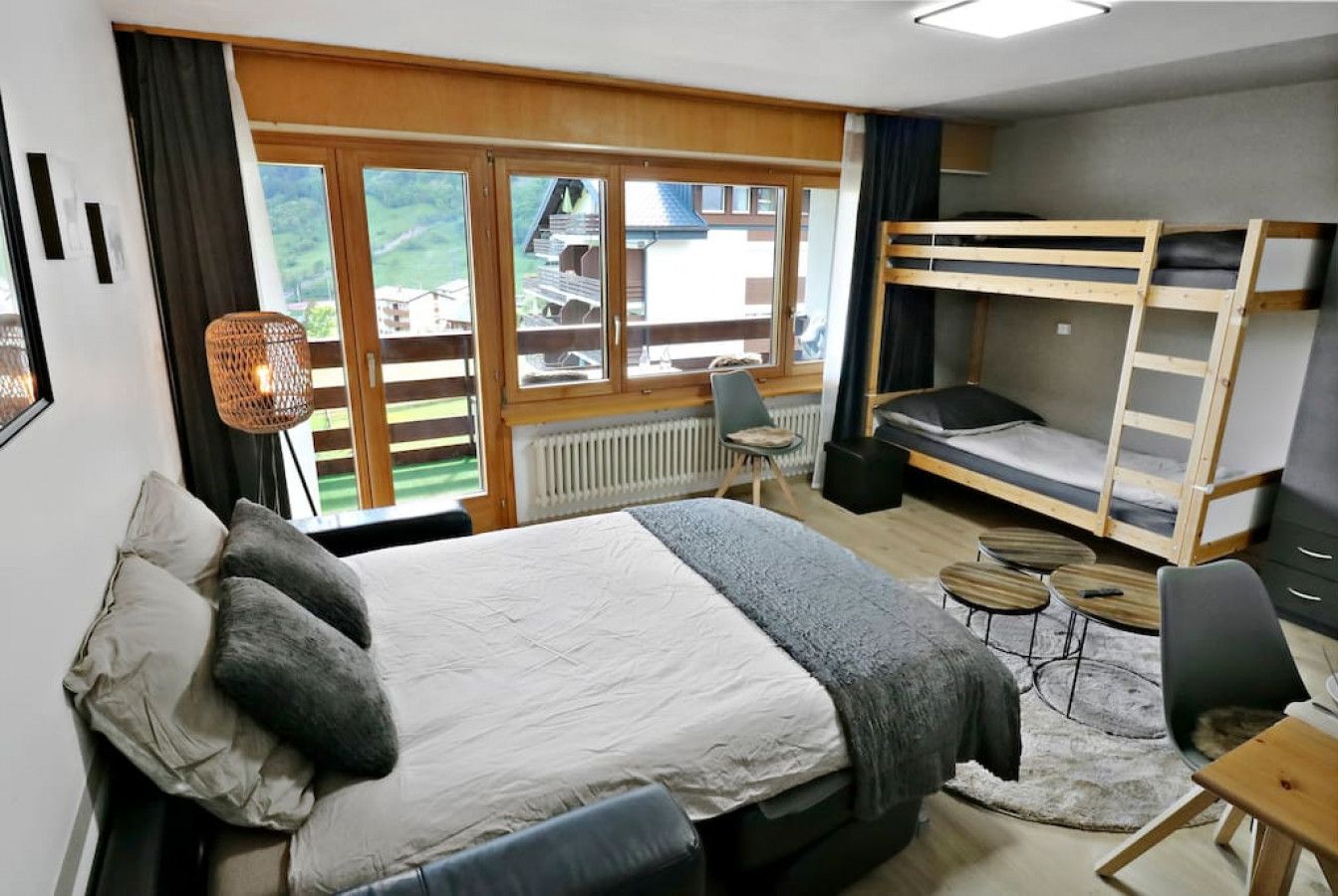 A bedroom with a bunk bed, a desk, a chair, a radiator, and a view of the outdoors.