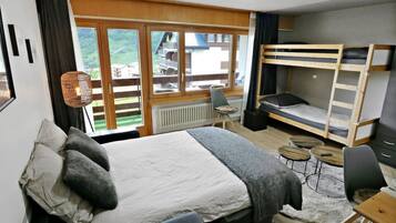 A bedroom with a bunk bed, a desk, a chair, a radiator, and a view of the outdoors.
