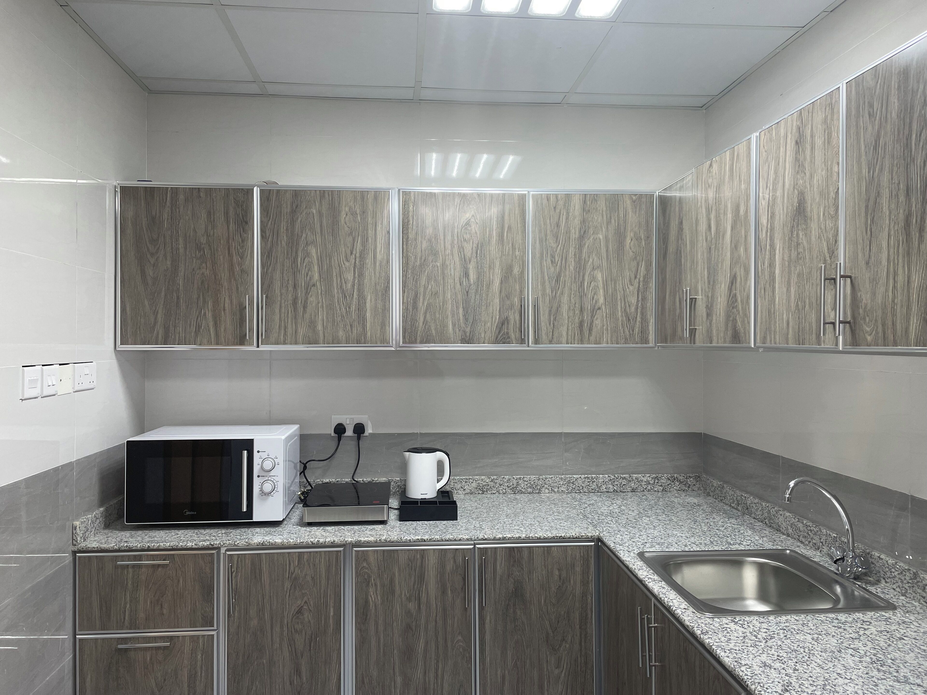 A modern kitchen with grey cabinets, a built-in microwave, a kettle, and a sink.